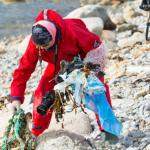 Personne en combinaison de protection ramassant les déchets sur une plage de galets